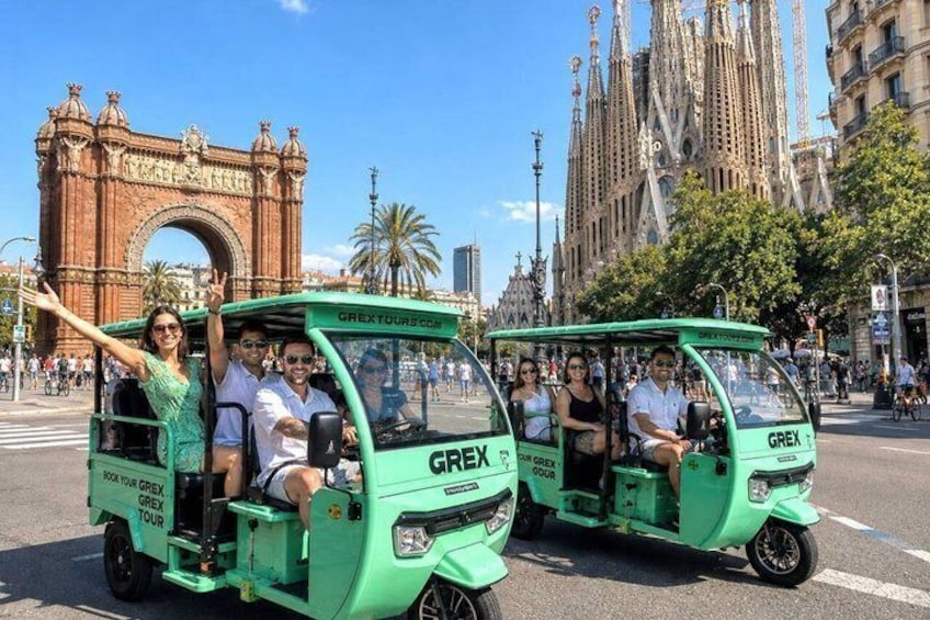 A green tour vehicle with passengers, a historic arch, and a cathedral in the background. 1