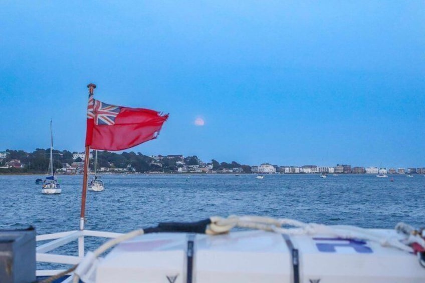 Un drapeau rouge sur un bateau, une eau calme et une côte lointaine parsemée de bâtiments. 5