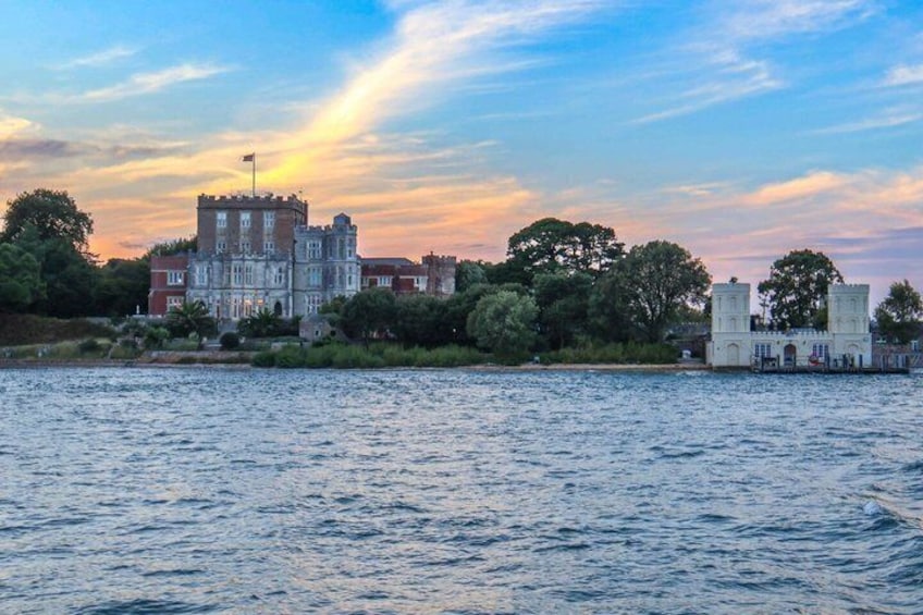 Un grand bâtiment historique doté d’une tour, situé au bord d’une étendue d’eau, sous un ciel embrasé par le coucher de soleil. 3