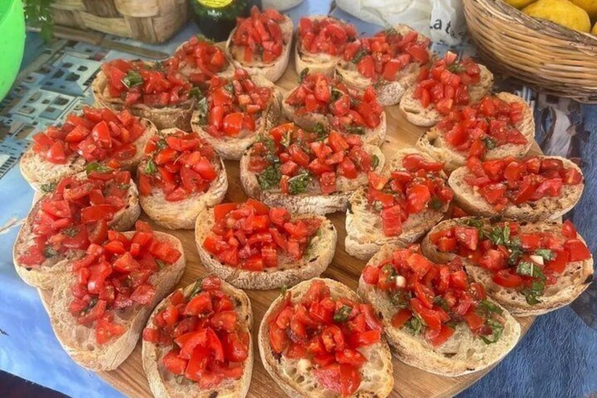 Ein Holzbrett mit mehreren Bruschetta-Scheiben, belegt mit gewürfelten Tomaten und Kräutern. 5