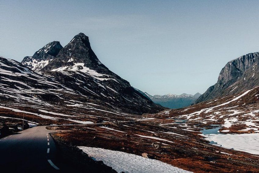 A winding mountain road with snow patches and rocky terrain. 2