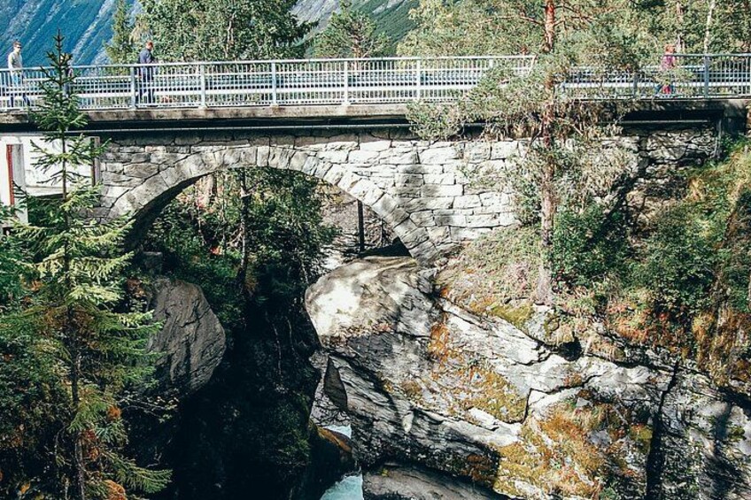 A stone bridge over a rocky gorge with a railing and people walking. 3