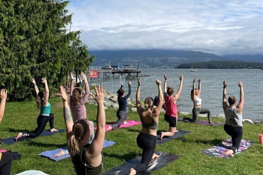 A group of people doing yoga on mats by a lake with a cityscape in the background. 1