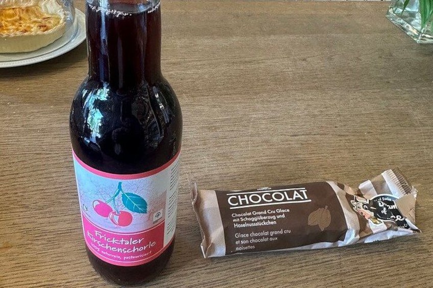 A bottle of dark liquid with a label featuring cherries and the word 'CHOCOLAT' and a chocolate bar beside it. 2