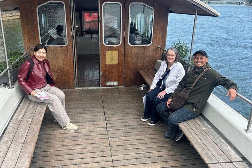 Three people sitting on a wooden deck of a boat with a wooden railing and windows. 5