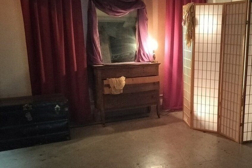 Una habitación con un aparador de madera, una ventana con cortinas moradas, una puerta cerrada y una maleta en el suelo. 2