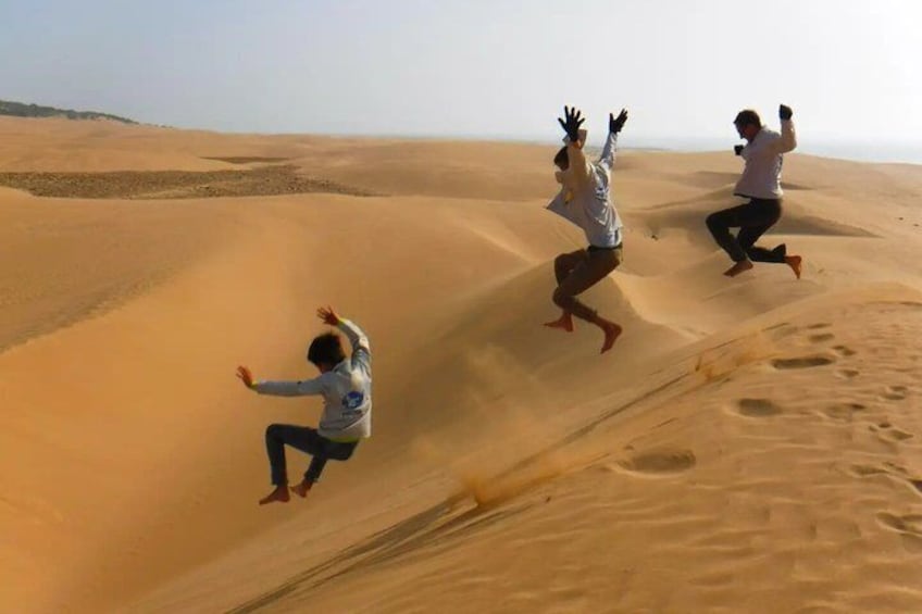 Drei Personen springen über eine Sanddüne. 4