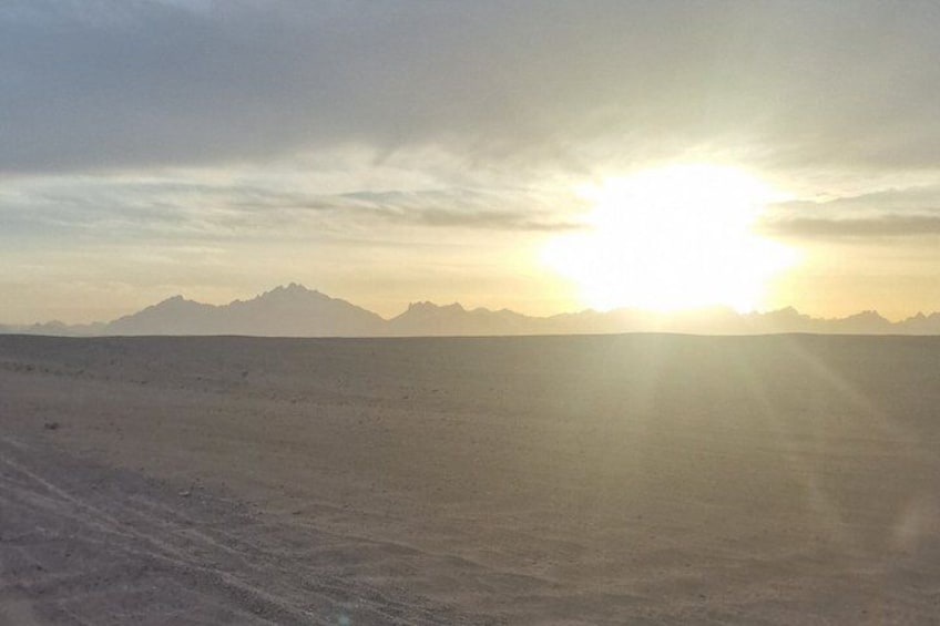Un paysage désertique avec une chaîne de montagnes à l’horizon et le soleil se couchant ou se levant. 2