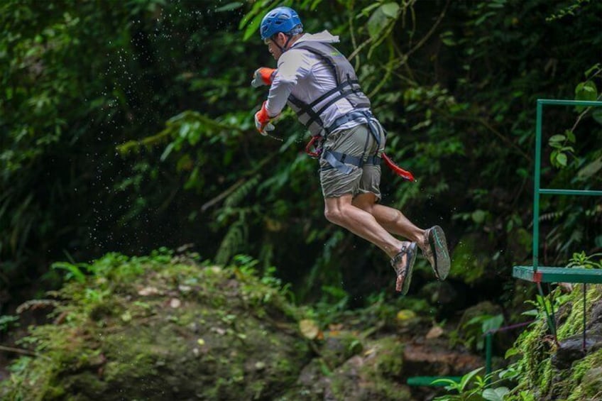Una persona saltando desde una plataforma verde en un área boscosa. 1