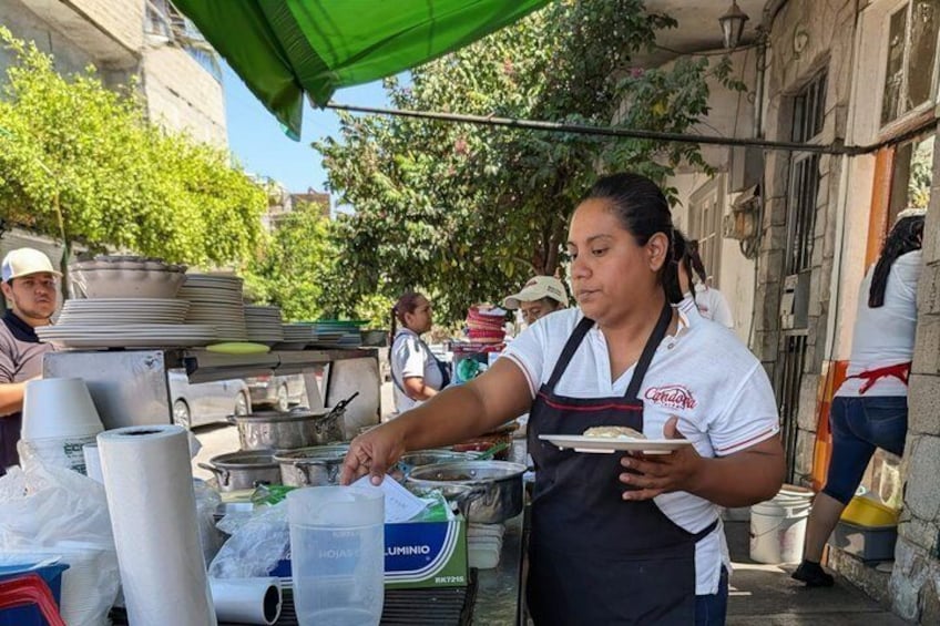 Straatverkoper bereidt eten buiten, met kookgerei en bakken in het zicht. 2