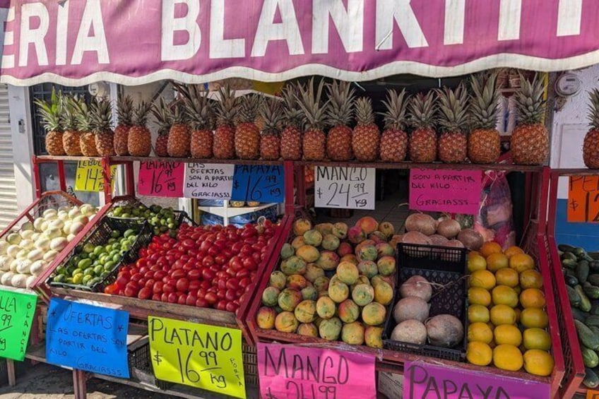 Een kraampje vol fruit, zoals ananassen, appels en bananen, met zichtbare prijzen. 3