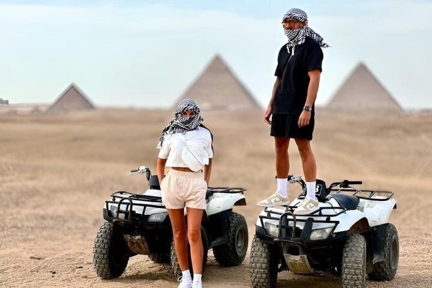 Två personer på fyrhjulingar i en öken med pyramider i bakgrunden. 4