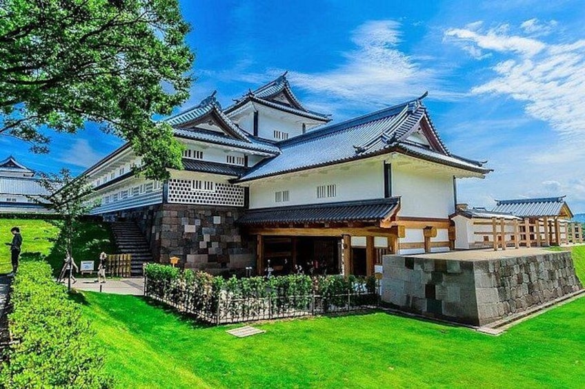 A traditional Japanese castle with multiple buildings, a well-maintained lawn, and a clear blue sky. 1