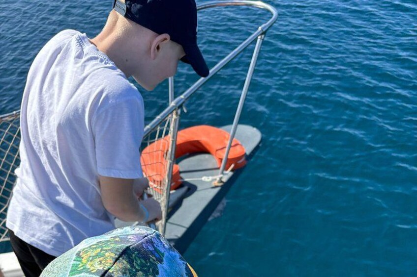 Eine Person in einem Boot, mit weißem T-Shirt und dunkler Mütze, die ein Gerät betrachtet. 2