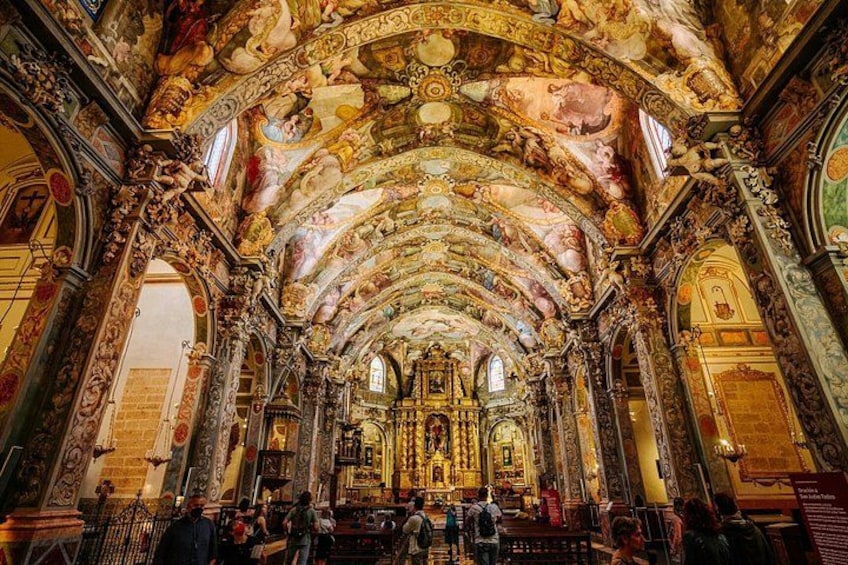 Interior de una iglesia ornamentada con un techo abovedado alto, frescos intrincados y un altar central. 1