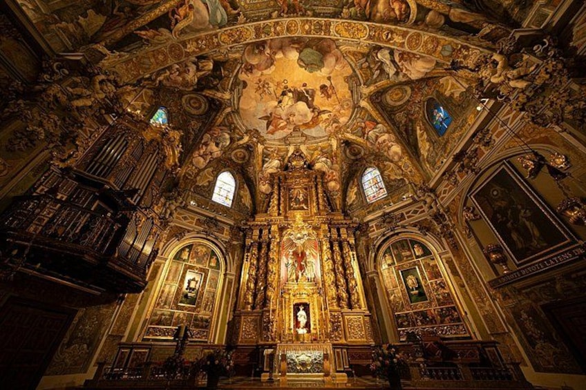 Interior de una iglesia ornamentada con un altar central, vidrieras de colores y frescos detallados en el techo. 3