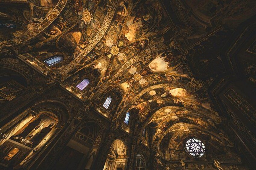 Un interior ornamentado con detalles arquitectónicos intrincados, incluyendo un amplio ventanal circular de vitrales y varios arcos. 2