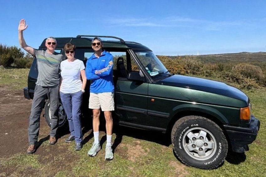Three people standing next to a green SUV on a grassy field with a clear sky. 1