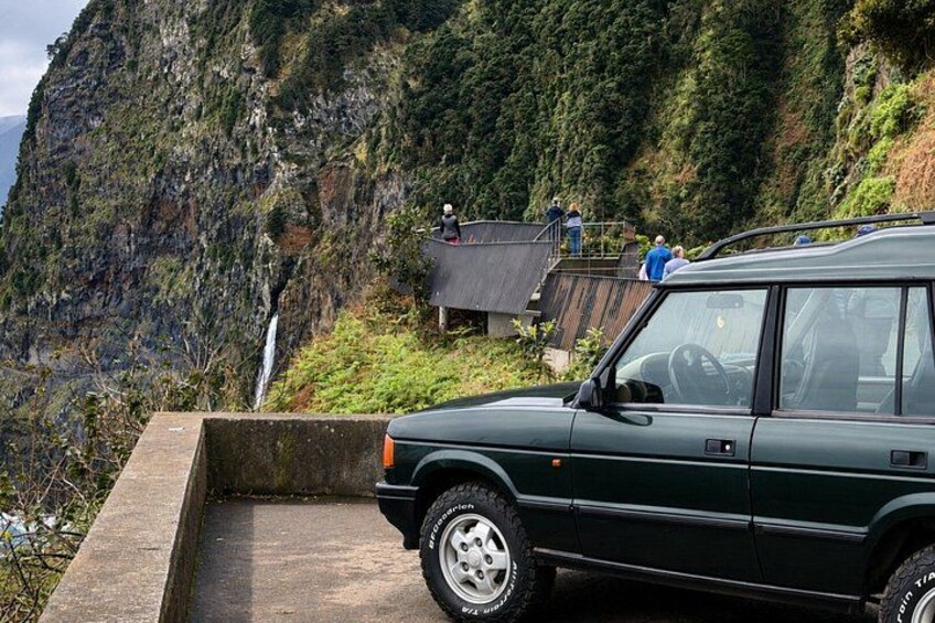 A green car parked on a concrete ledge with a mountainous landscape in the background. 5