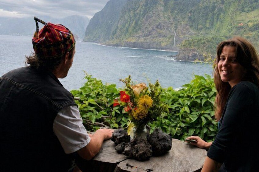 A person holding a bouquet of flowers, sitting at a table with a view of a coastal landscape. 2