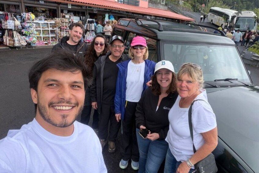 A group of people posing in front of a vehicle with a market in the background. 1