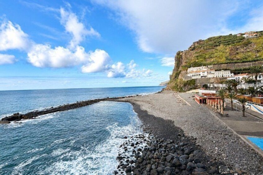 A rocky beach with a breakwater, calm sea, and buildings on a hillside. 5