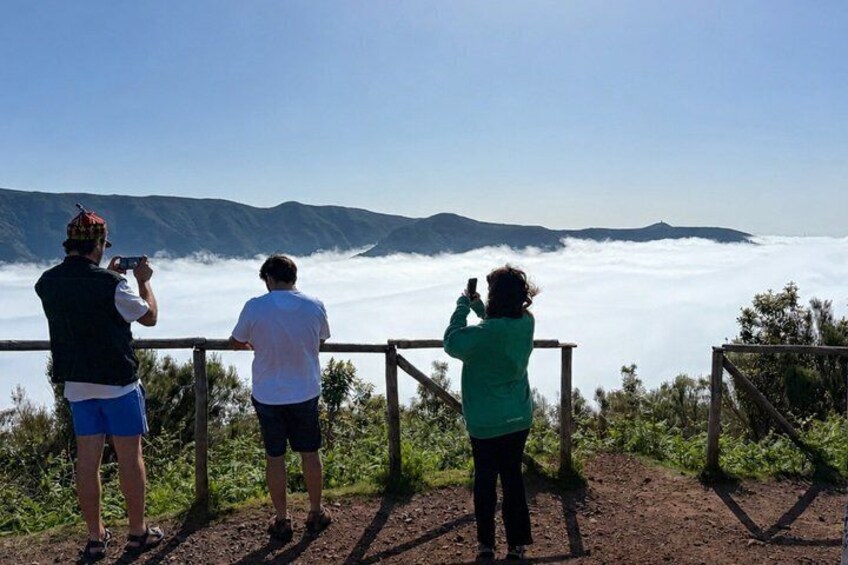Three people taking photographs of a mountain range with a cloud-covered valley below. 3