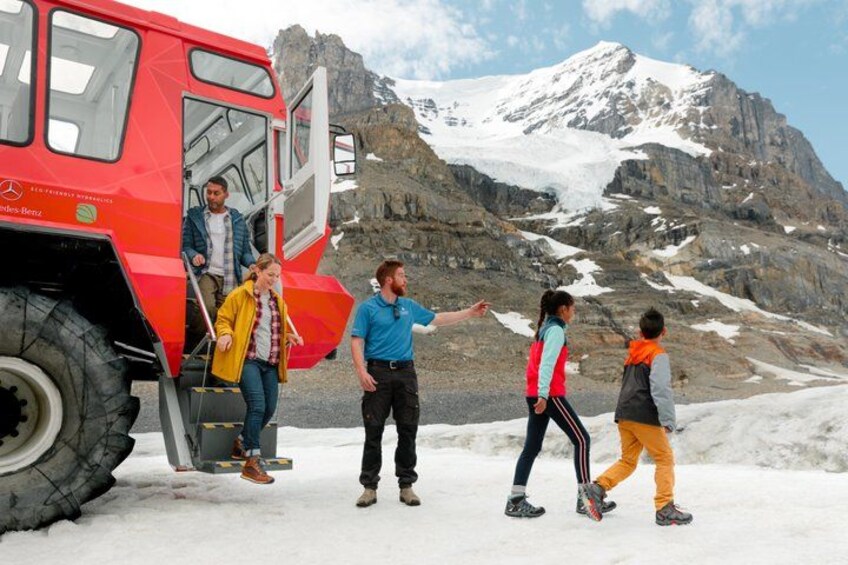 Un groupe de personnes monte à bord d’un autobus rouge, avec un paysage montagneux enneigé en arrière-plan. 5