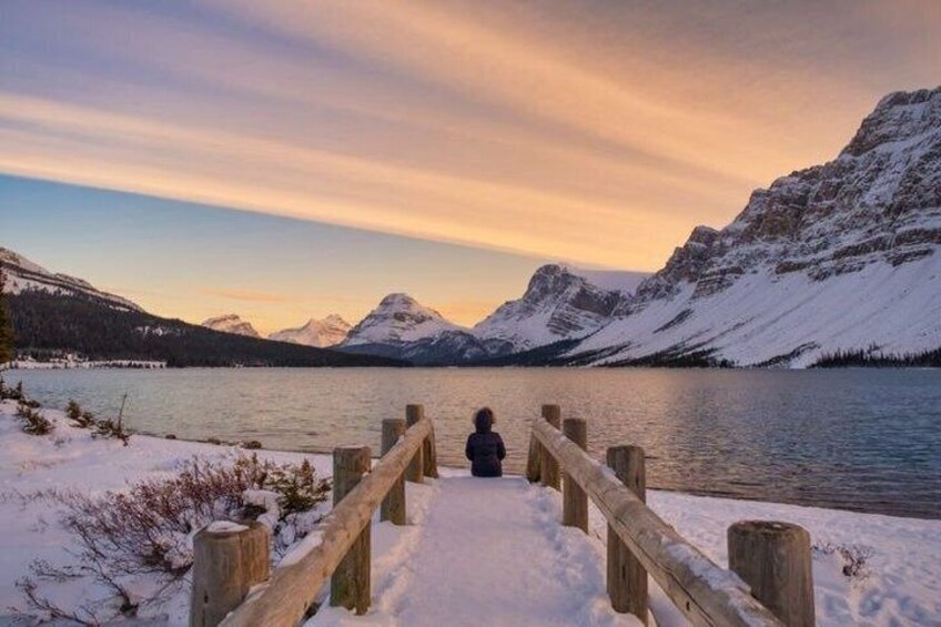 Een houten steiger die uitkomt op een kalm meer, met besneeuwde bergen op de achtergrond. 3