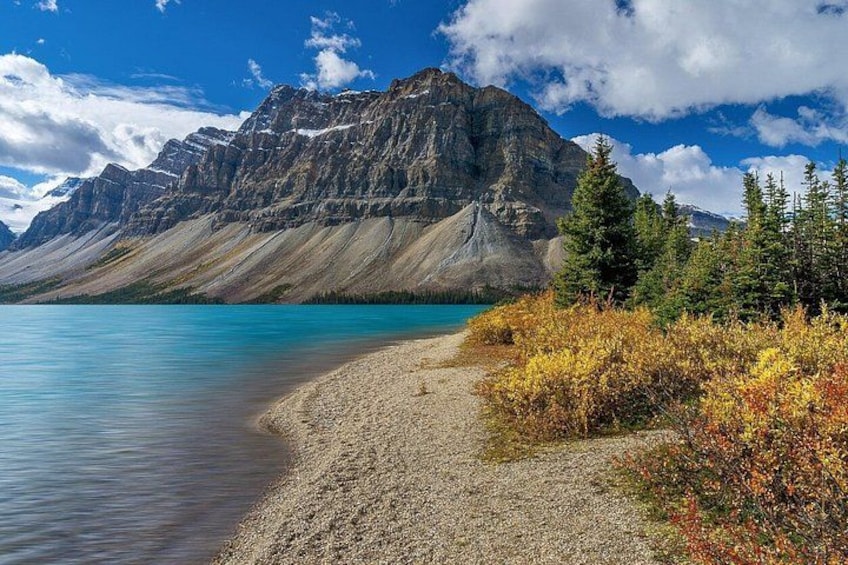 A mountain landscape with a clear lake, a gravel path, and autumn foliage. 1