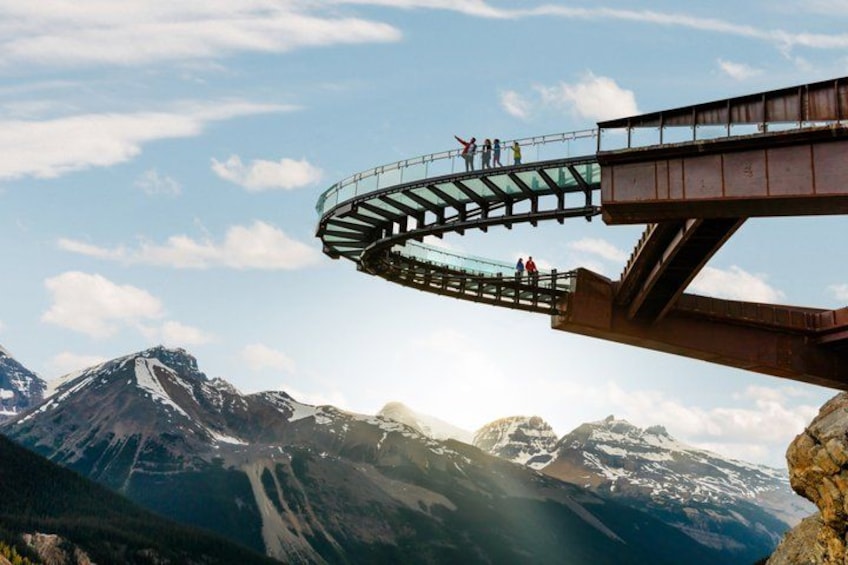 Un pont de verre sur lequel des personnes se promènent, entouré de montagnes et surplombant un ciel dégagé. 1