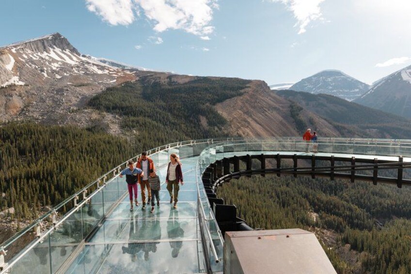 Un pont de verre sur lequel des personnes se promènent, entouré de montagnes et d’une forêt. 3