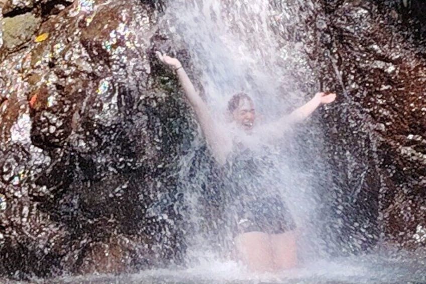 A person standing in a waterfall with arms raised. 2