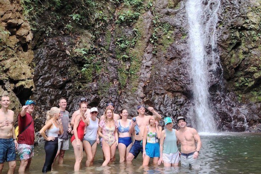 A group of people standing in shallow water with a waterfall in the background. 1