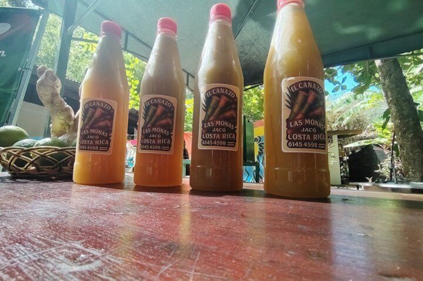 Four bottles of 'Las Monas' juice on a table with a tropical background. 5
