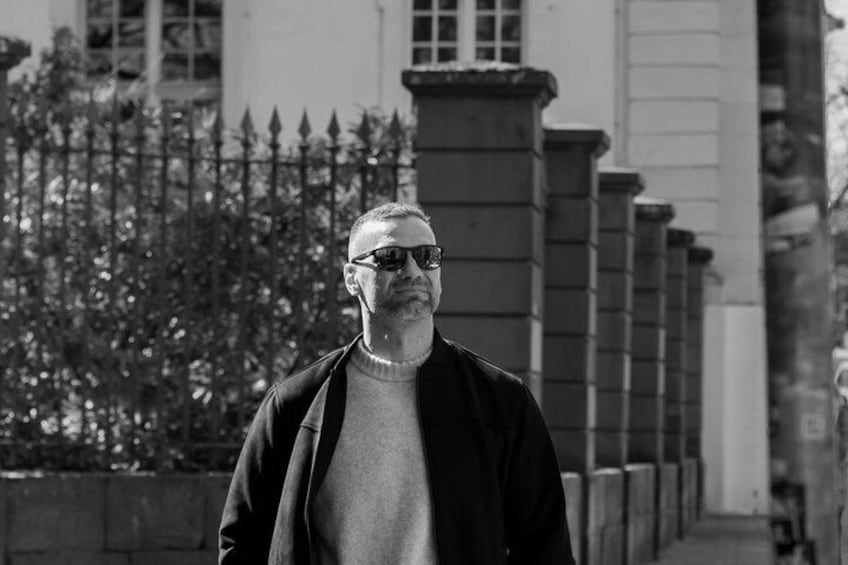 Un homme marchant sur un trottoir, avec un bâtiment et une clôture en arrière-plan. 3