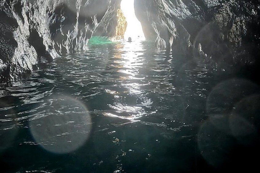 A cave with water reflecting sunlight, a narrow opening, and a rough cave wall. 4