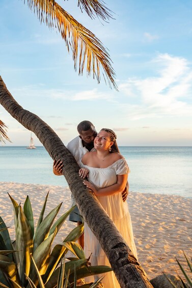 A couple embracing on a beach with a palm tree and ocean in the background. 3