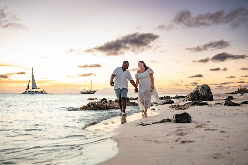 A couple walking on a beach with a sailboat in the background. 5