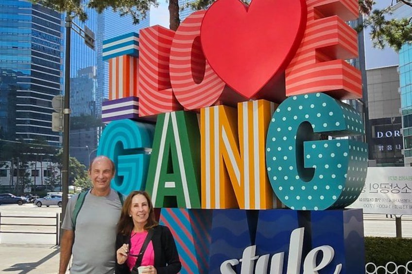 Een groot, kleurrijk bord met de tekst 'LOVE GANG' en 'style', in een stadsgezicht met gebouwen op de achtergrond. 5