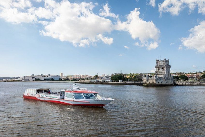 Un barco rojo y blanco sobre aguas tranquilas, una torre histórica al fondo y un cielo azul despejado con nubes. 5