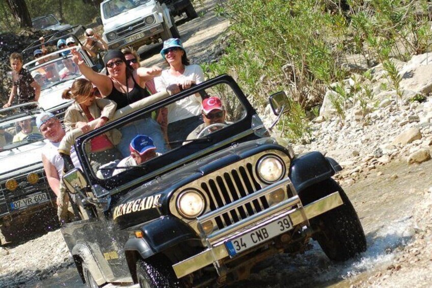 A vintage jeep with passengers, driving through a rocky terrain. 4