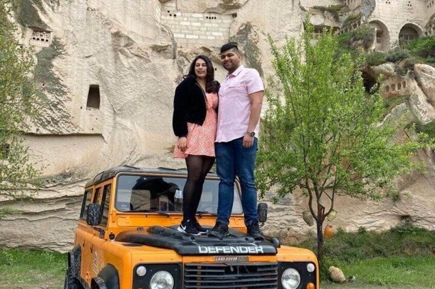 A couple standing on a Defender vehicle in front of a rock formation. 2