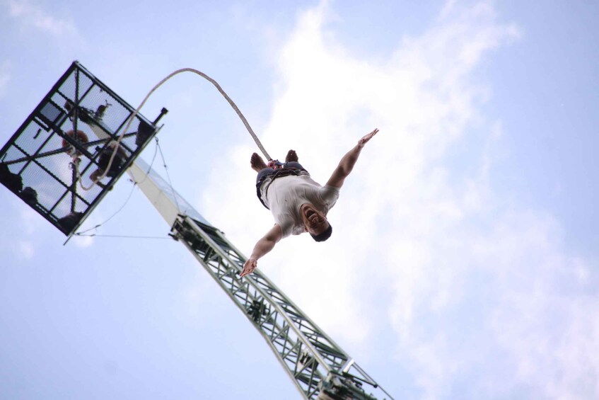 A person performing a bungee jump from a tall structure against a clear sky. 5