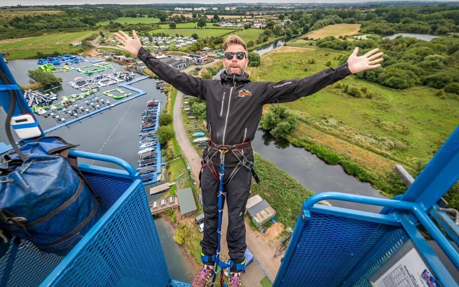 A person bungee jumping from a high platform with arms outstretched, overlooking a river and surrounding landscape. 3