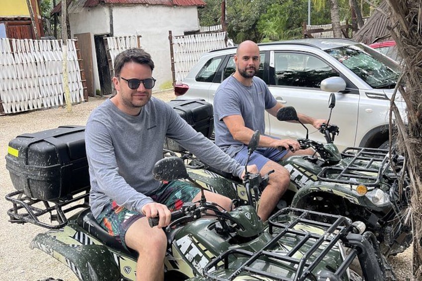 Dos personas en vehículos todo terreno, un coche y una valla al fondo. 3