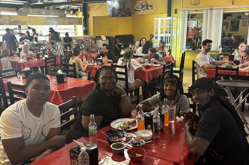 Un grupo de personas comiendo en mesas en una cafetería con manteles rojos. 1