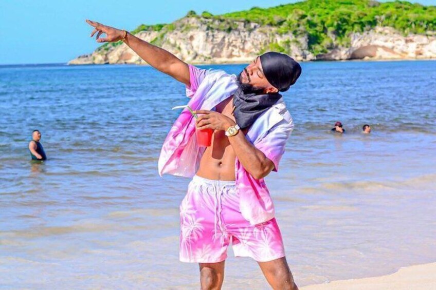 A person in a pink and white outfit standing on a beach with a clear sky and rocky cliffs in the background. 4