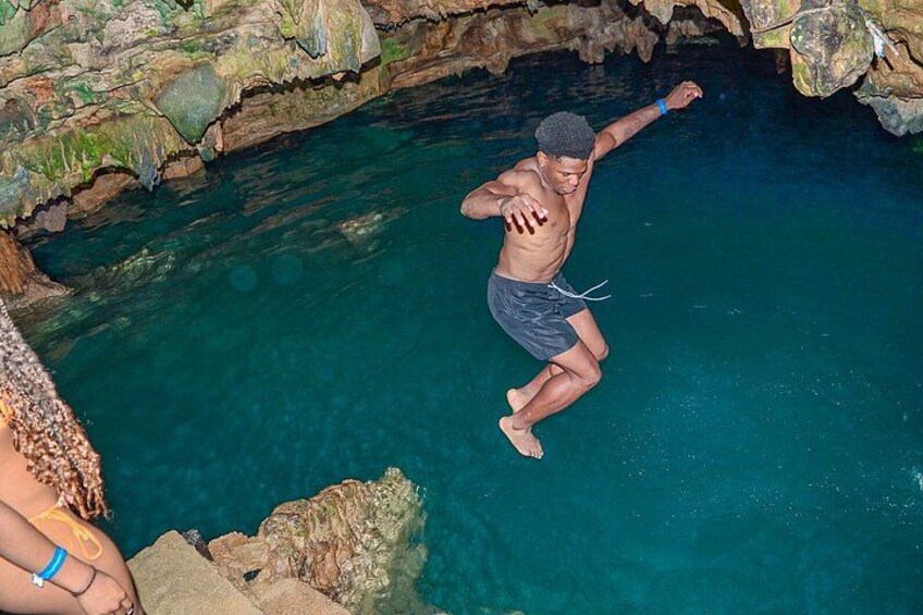 A person jumping into a clear blue pool surrounded by rocky terrain. 1
