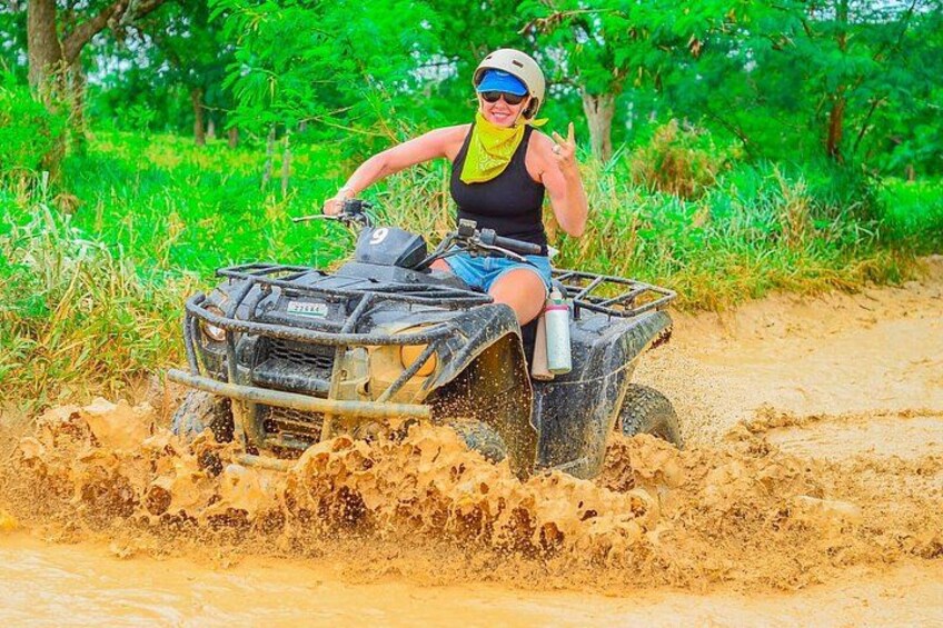 A person riding an ATV through a muddy area with trees in the background. 2